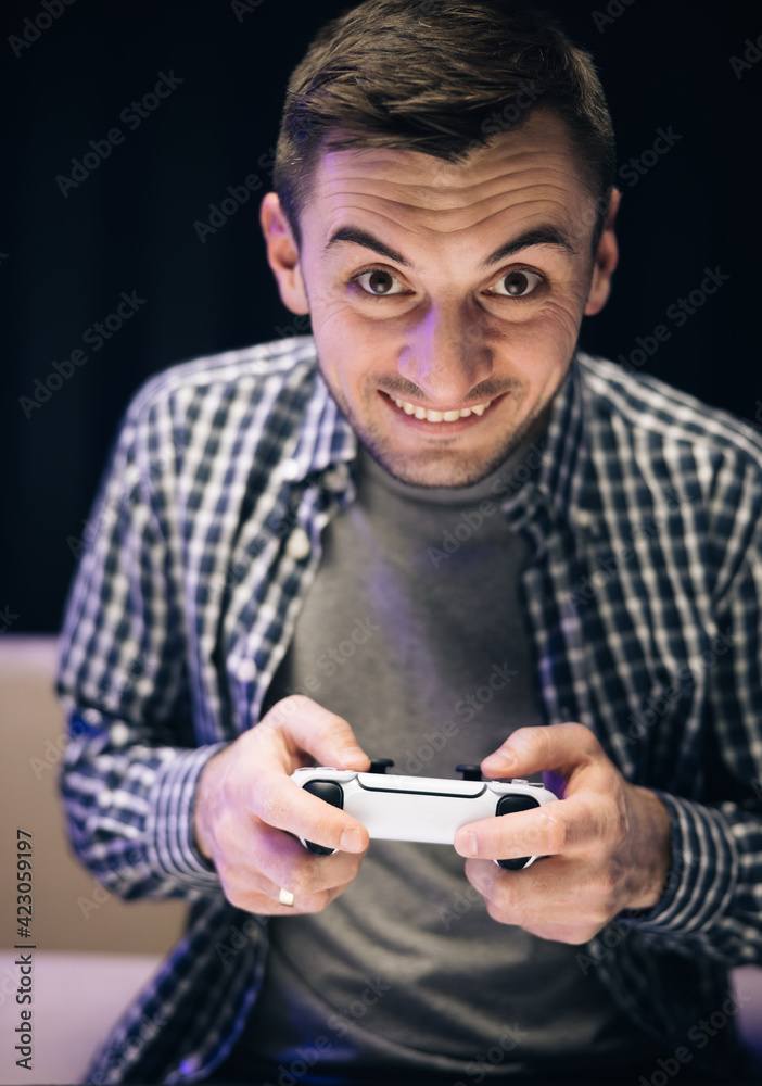 Man in casual wear playing video game in home living room. Caucasian guy holding joystick control having fun laughing on couch indoors Man in casual wear playing video game in home living room. Caucasian guy holding joystick control having fun laughing on couch indoors
