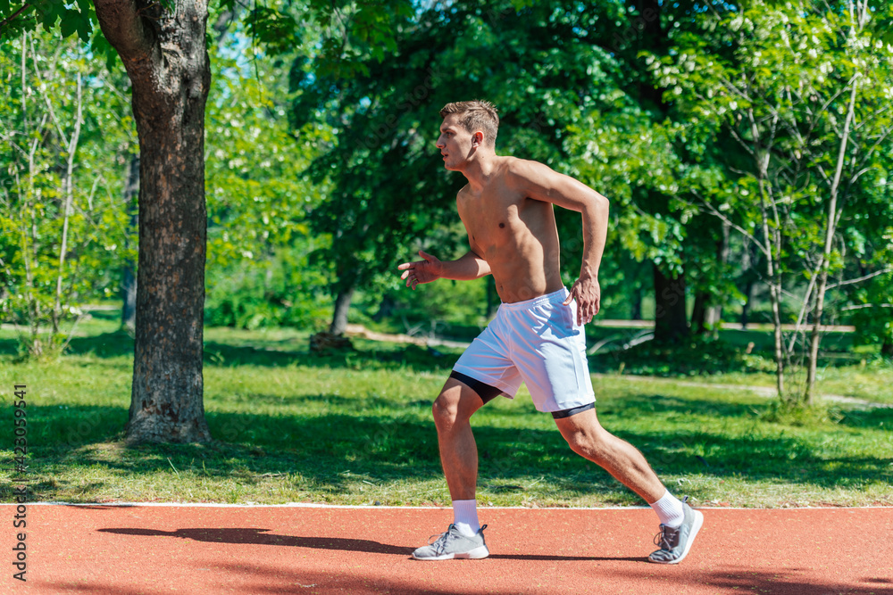 Side view of a strong attractive man running shirtless outside in the park