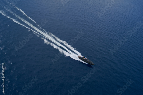 Drone view of a dark blue boat. Aerial view luxury motor boat. Drone view of a boat the blue clear waters. Large speed boat moving at high speed side view.