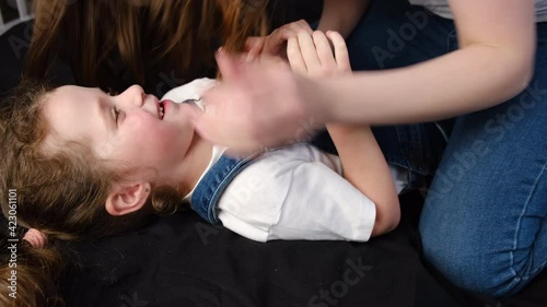 Close up of cheerful mommy tickling laughing small child daughter, having fun together on bed at home. Playful young mum with overjoyed emotional little kid girl, enjoying spending free weekend time
