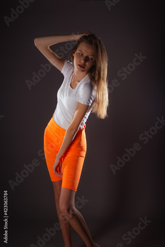 Pretty sports girl with short orange leggings posing isolated on dark background in studio photo