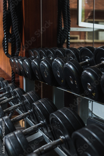 Heavy black dumbbells with metal bars and plates reflecting in mirror in gymnasium in daytime