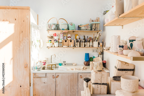 Studio with wooden shelves with different instruments for pottery and utensil near sink in daylight