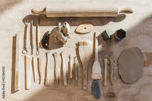 Top view of set of various tools for pottery with loops and stacks with paintbrushes and rolling pin with piece of smoothed clay placed on wooden table in workshop photo