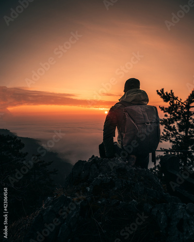 Hiker with backpack standing on top of a mountain and enjoying sunrise.