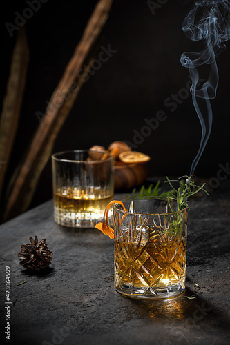 Crystal glass of old fashioned whiskey drink garnished with fresh rosemary and orange peel on black table