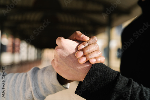 Side view of unrecognizable stylish young diverse male friends in trendy outfits standing on paved street in city and shaking hands photo