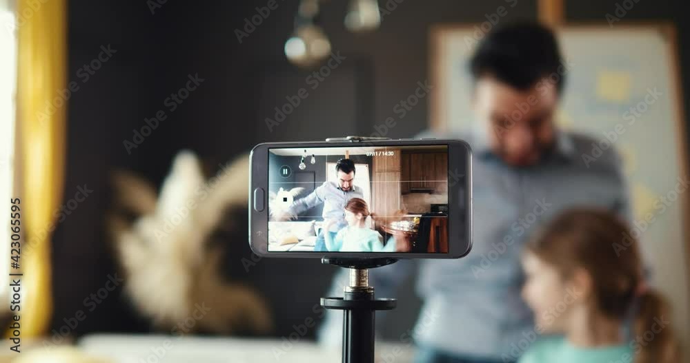 Dad and daughter are having fun recording a video blog on their phone. Happy family streamers are shooting their blog at the smartphone camera. Theme of family blogging and making streams Dad and daughter are having fun recording a video blog on their phone. Happy family streamers are shooting their blog at the smartphone camera. Theme of family blogging and making streams