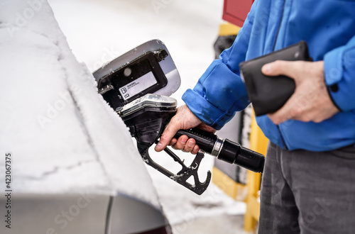 Man holding fuel nozzle, filling gas tank of diesel car covered with snow