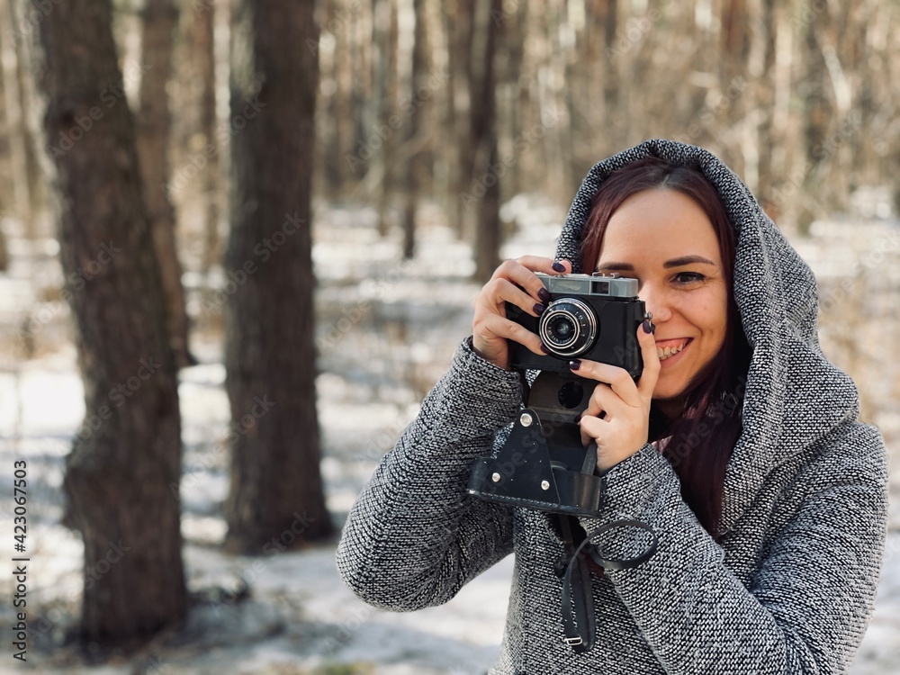 Young woman in gray coat photographing on old photo camera in forest. Pretty female taking photos with old camera in early spring. Young woman in gray coat photographing on old photo camera in forest. Pretty female taking photos with old camera in early spring.
