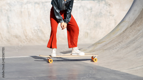 Crop anonymous female in stylish wear riding longboard during training in skate park photo