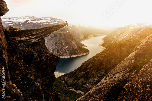 Distance view of explorer sitting on edge of Trolltunga rock formation at sunset during vacation in Norway photo