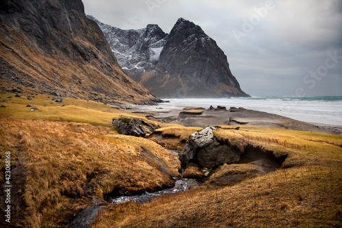 Amazing landscape of small river flowing in sea with mountains on shore under cloudy sky in Norway