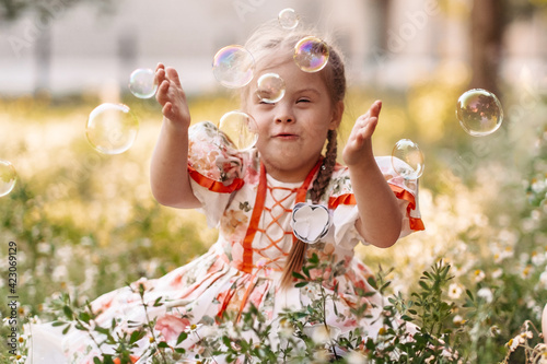 A girl with Down syndrome blows bubbles. The daily life of a child with disabilities. Chromosomal genetic disorder in a child.