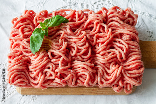 From above of fresh raw mixed pork and beef minced meat on wooden cutting board with green basil leaves placed on table during cooking process