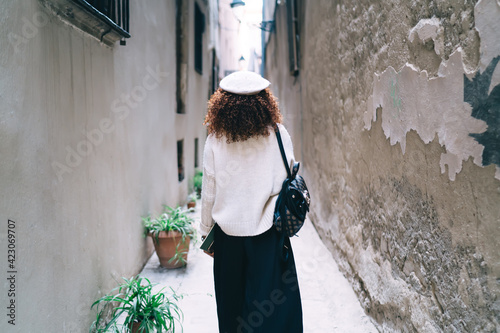 Back view of dark skinned curly woman traveler walking on city street on free time vacations,rear view of african american traveler strolling on urban settings explore location and destination in town #423069707