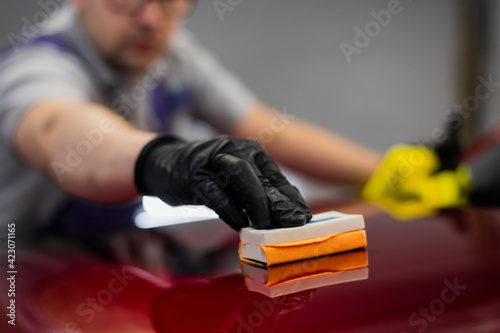 Close-up man applying ceramic coating on the red car at detailing service.