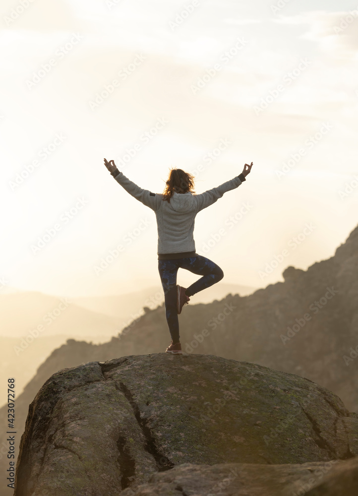 Back view of unrecognizable female standing on top of rocky mountain and doing Tree with Arms Up pose during sunset Back view of unrecognizable female standing on top of rocky mountain and doing Tree with Arms Up pose during sunset