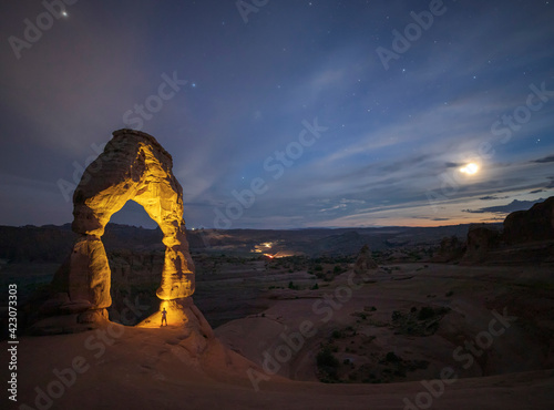 Amazing landscape with arched formation in red rock near rare vegetation located in national park against cloudy sky in USA