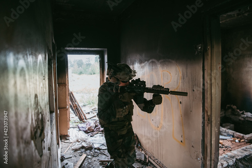 Soldier in full US MARSOC armed with assault rifle run through the abandoned building. Military clash. photo