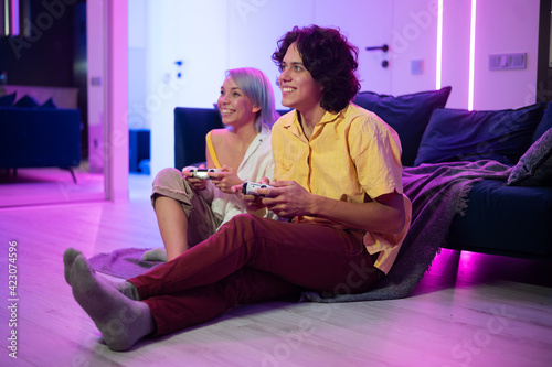 Smiling couple holding gamepads playing video game at home. Low angle shot of young people spending time together during self isolation on pandemic.