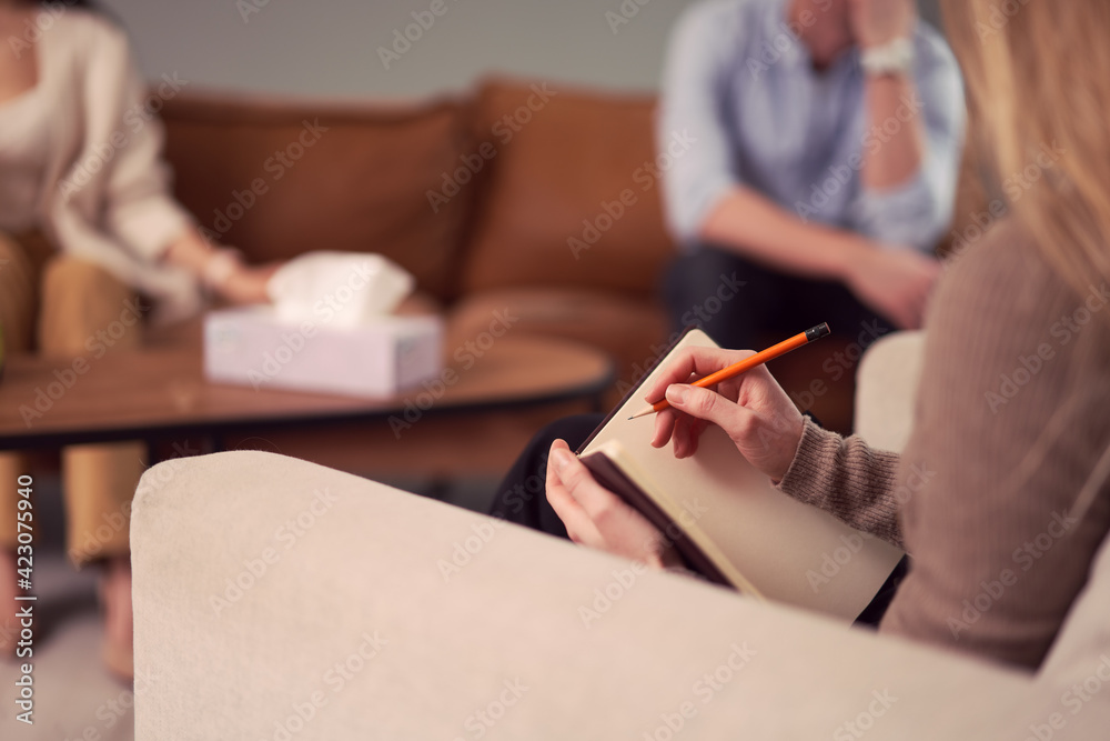 © Sergey Mironov/ADDICTIVE STOCK - Unrecognizable female psychologist talking notes in notebook during therapy session with couple in office