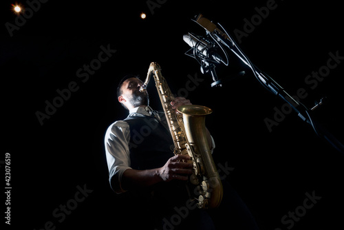 From below crop of male musician in classy outfit standing near microphone and playing alto saxophone during jazz concert photo