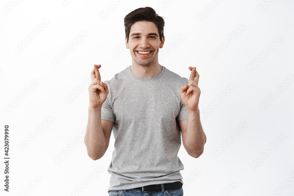 Luck. Hopeful man cross fingers for good luck, making wish, anticipating good news, waiting for results, smiling and looking optimistic, standing against white background Luck. Hopeful man cross fingers for good luck, making wish, anticipating good news, waiting for results, smiling and looking optimistic, standing against white background