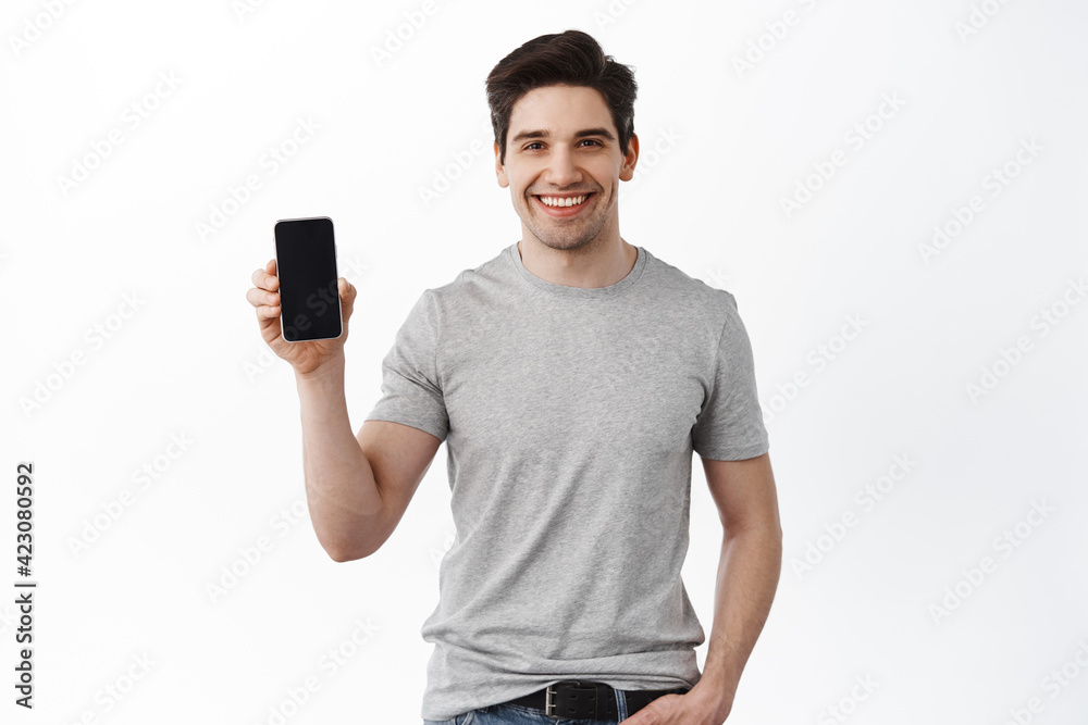 Caucasian handsome man show mobile phone screen, smiling and giving app recommendation, standing in t-shirt against white background Caucasian handsome man show mobile phone screen, smiling and giving app recommendation, standing in t-shirt against white background