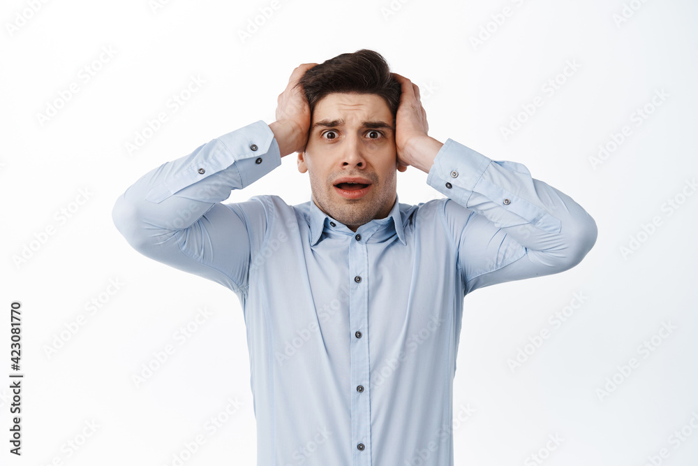 Scared and worried office manager, man in shirt panicking, holding hands on head and look nervous, standing over white background Scared and worried office manager, man in shirt panicking, holding hands on head and look nervous, standing over white background