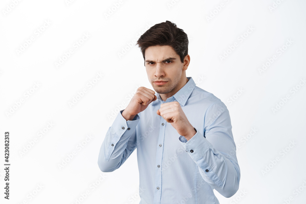 Wanna fight. Serious office worker in shirt raising fists, standing in boxer pose defensive, shadow boxing, standing over white background Wanna fight. Serious office worker in shirt raising fists, standing in boxer pose defensive, shadow boxing, standing over white background