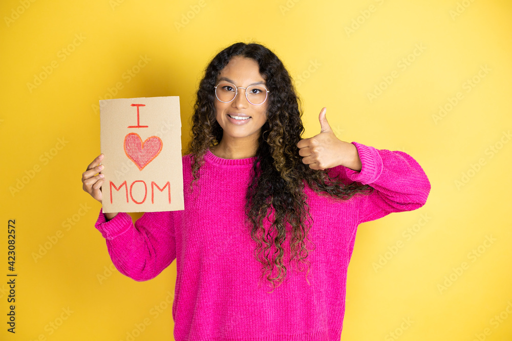 Beautiful woman celebrating mothers day holding poster love mom message doing positive gesture with hand, thumbs up smiling and happy. cheerful expression and winner gesture. Beautiful woman celebrating mothers day holding poster love mom message doing positive gesture with hand, thumbs up smiling and happy. cheerful expression and winner gesture.