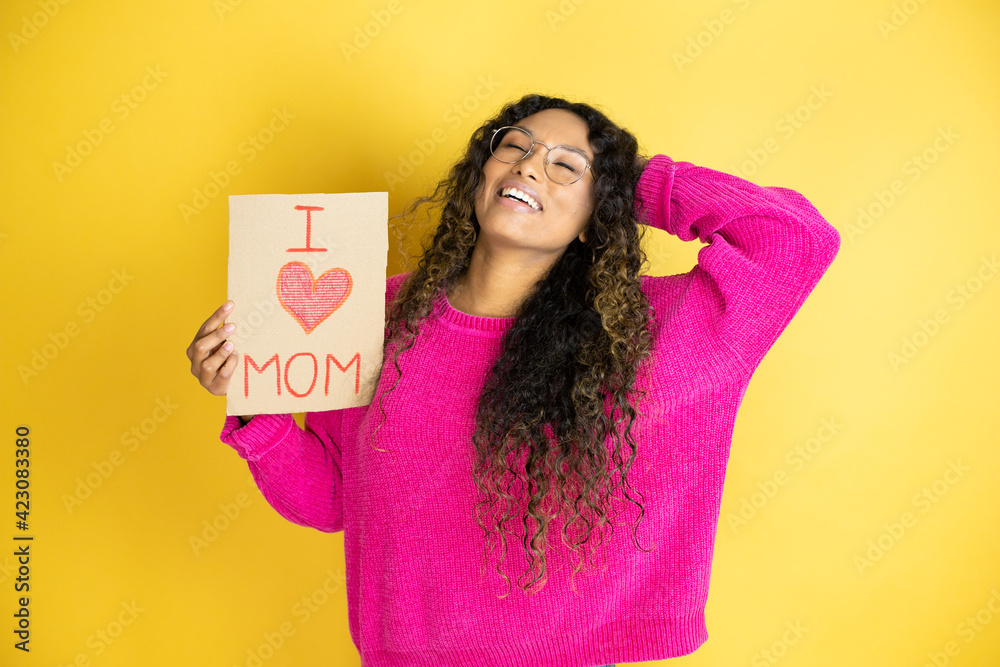 Beautiful woman celebrating mothers day holding poster love mom message relaxing and stretching, arms and hands behind head and neck smiling happy Beautiful woman celebrating mothers day holding poster love mom message relaxing and stretching, arms and hands behind head and neck smiling happy