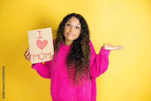 Beautiful woman celebrating mothers day holding poster love mom message clueless and confused expression with arms and hands raised