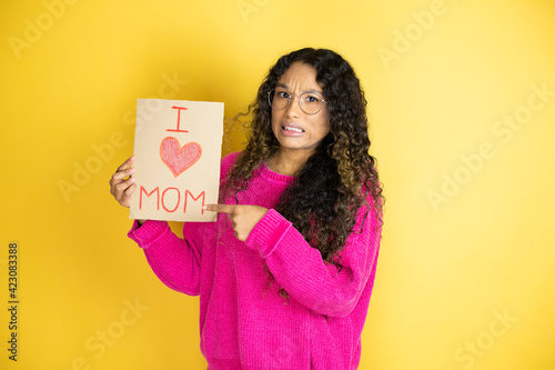 Beautiful woman celebrating mothers day holding poster love mom message scared and pointing with hand and finger