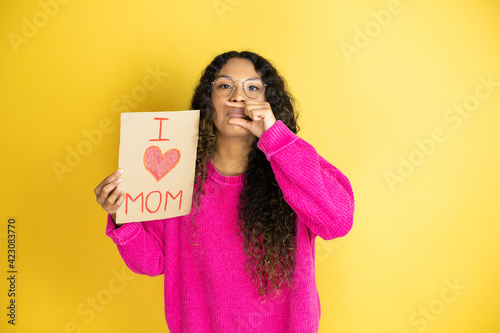 Beautiful woman celebrating mothers day holding poster love mom message mouth and lips shut as zip with fingers. Secret and silent, taboo talking