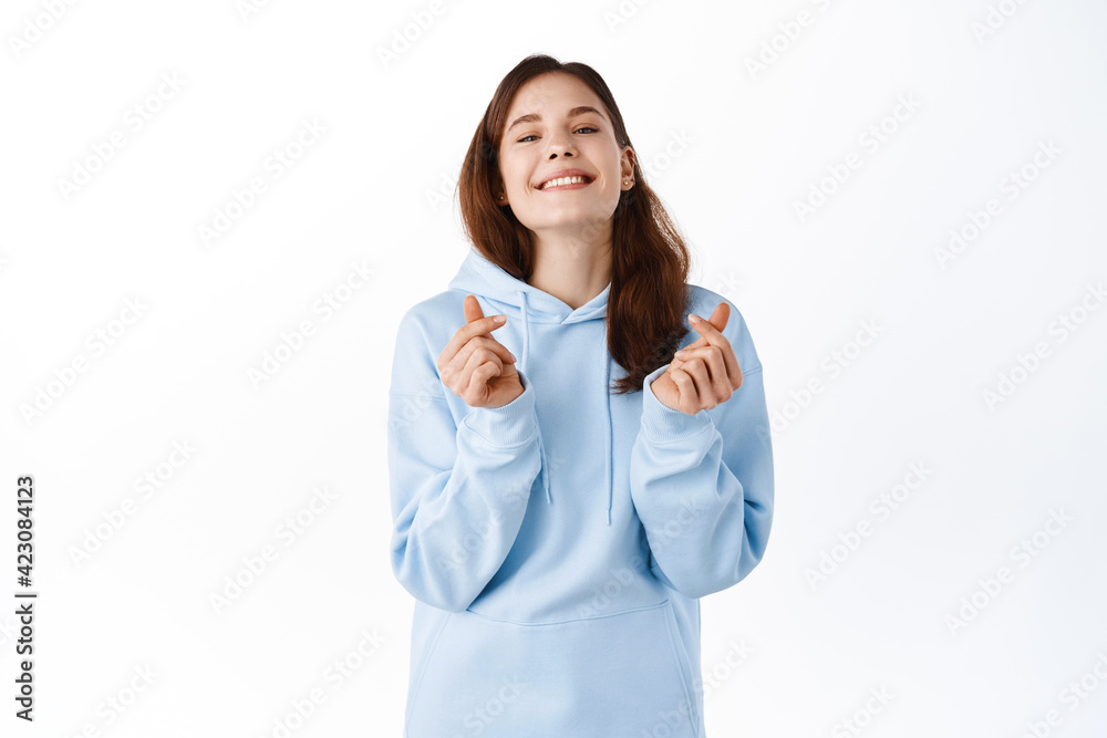 Beautiful young woman in casual blue hoodie, showing finger hearts and smiling cute at camera, positive emotions concept, standing over white background Beautiful young woman in casual blue hoodie, showing finger hearts and smiling cute at camera, positive emotions concept, standing over white background