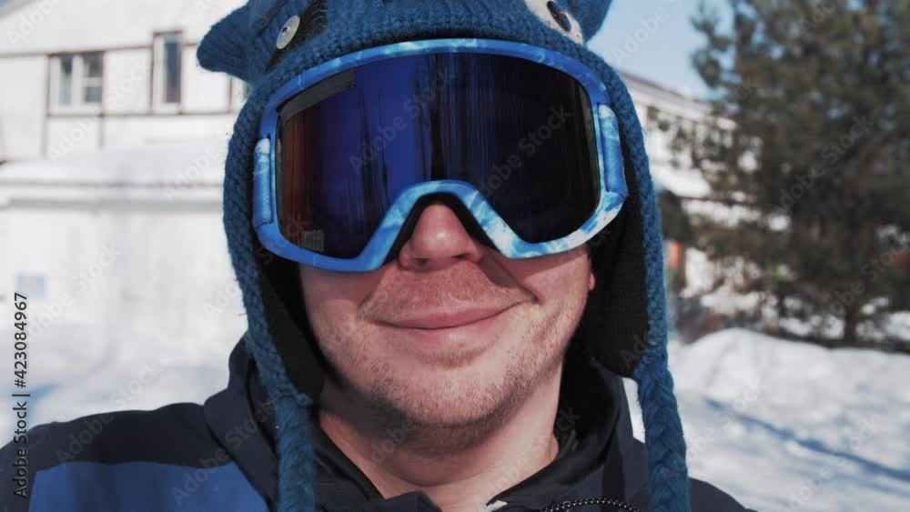 Close-up portrait of laughing cheerful and happy snowboarder, skier in a ski goggles and in a funny hat. Sunny day at the ski resort. Close-up portrait of laughing cheerful and happy snowboarder, skier in a ski goggles and in a funny hat. Sunny day at the ski resort.