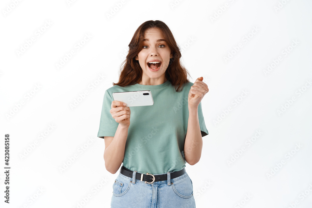 Happy attractive brunette girl joying win in video game on smartphone, isolated over white background Happy attractive brunette girl joying win in video game on smartphone, isolated over white background