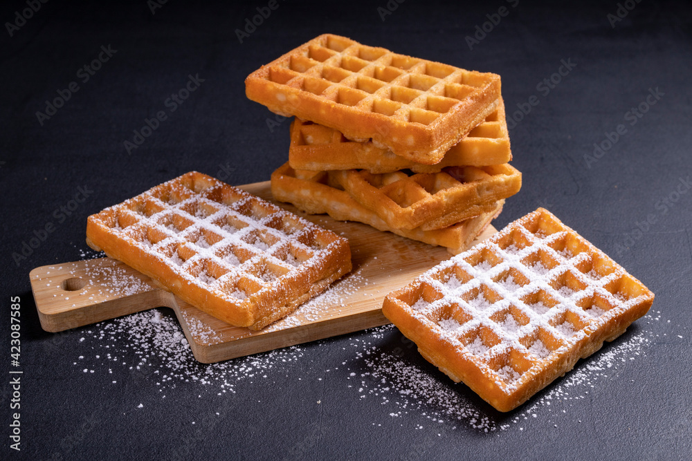 Sweet waffles sprinkled with powdered sugar prepared for serving. A tasty dessert eaten with fruit and preserves. Sweet waffles sprinkled with powdered sugar prepared for serving. A tasty dessert eaten with fruit and preserves.