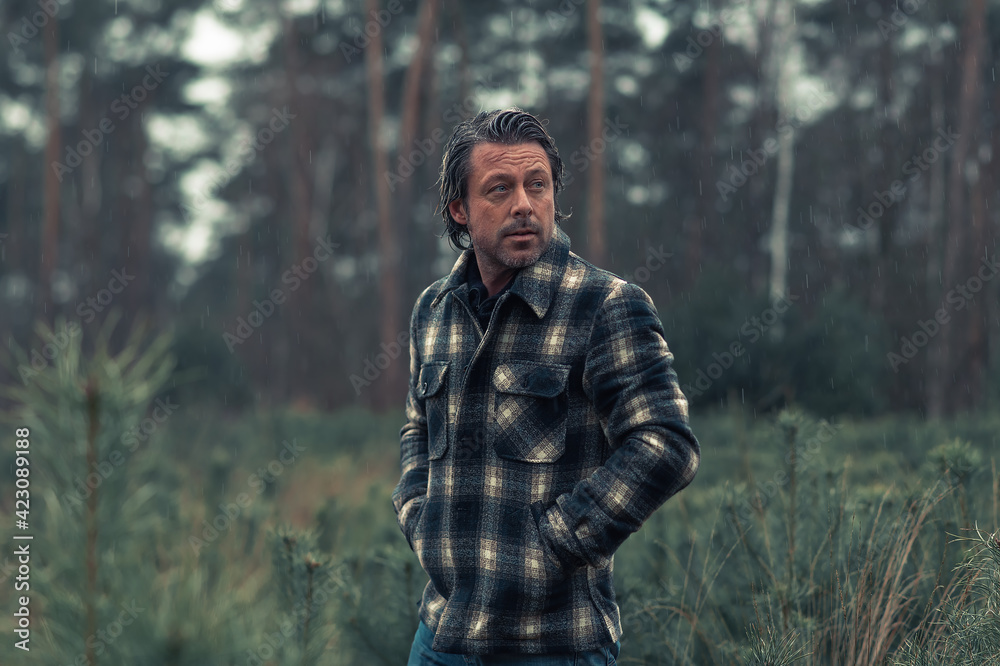 Obraz premium Man with stubble beard in a checkered coat in a rainy woodland.
