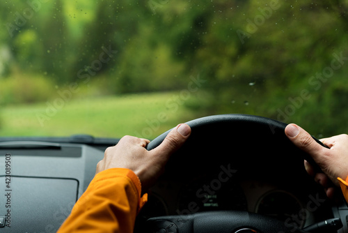 Close up image of Driver's hands on steering wheel driving a modern off road right hand drive RHD car on the mountain green forest country road. Inside car windshield view point. Auto driving concept. photo