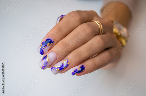 A well-groomed female hand on a white background, a manicure with a blue and light gel polish with the addition of gold.