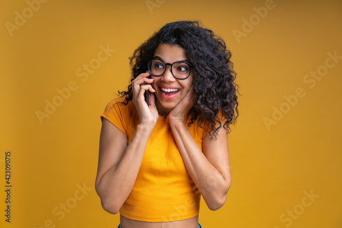 Portrait of smiling girl talking to her friends on smartphone isolated over yellow background