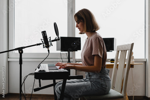 young woman playing piano and singing a song at homestudio photo