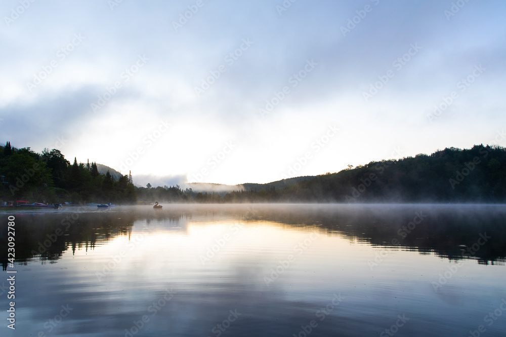 plan large d'un lac calme miroitant le ciel lors d'un lever de soleil brumeux