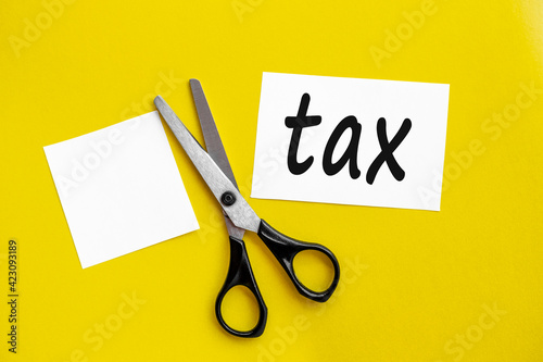 Cut taxes concept. Sciccors cut paper with word Taxes on yellow background top view.