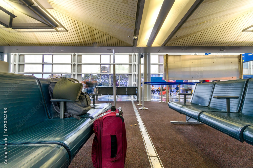 A backpack and a rolling suitcase sit by the benches of an airport terminal lounge.