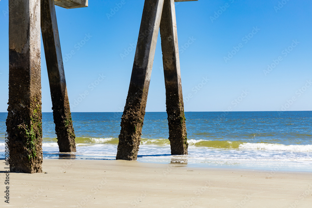 Barnacle covered concrete pier pilings by blue ocean waters, bright blue sky, horizontal aspect