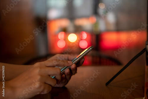 smartphone in hand,playing the smartphone in coffee shop,take showing bokeh behind the candle light, take in Phon ,Khonkean,Thailand ,19 mach 2021 photo